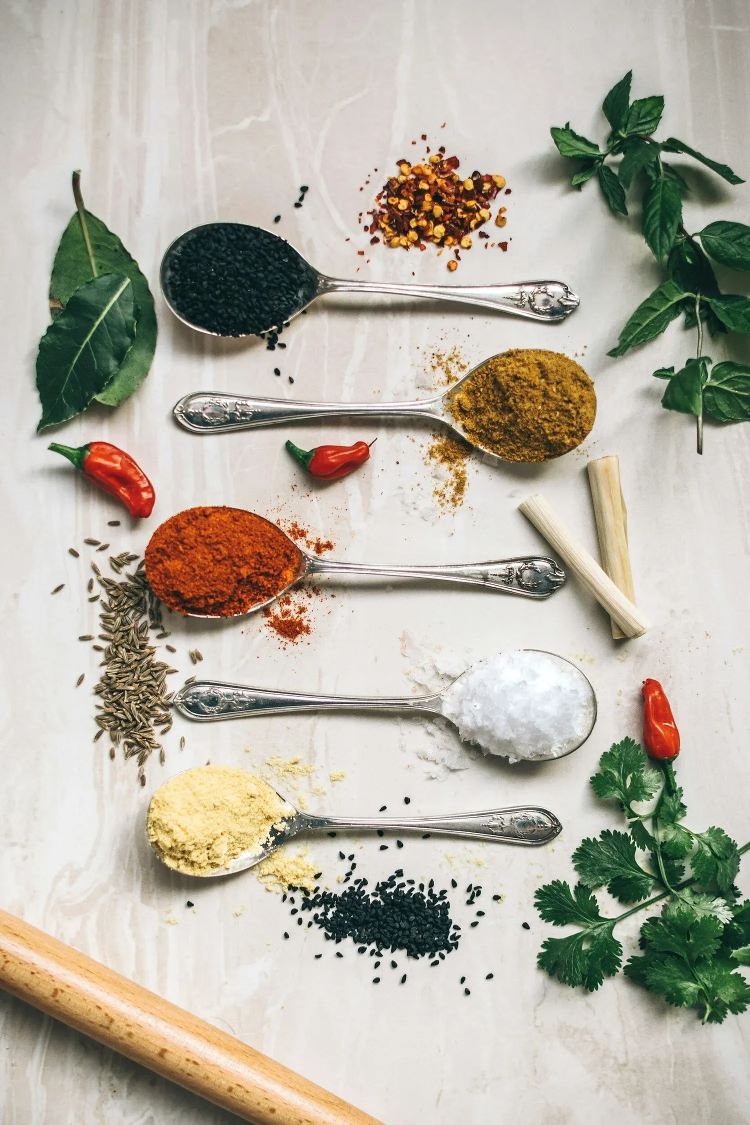 Spoons of colorful herbs and spices laid out with fresh leaves