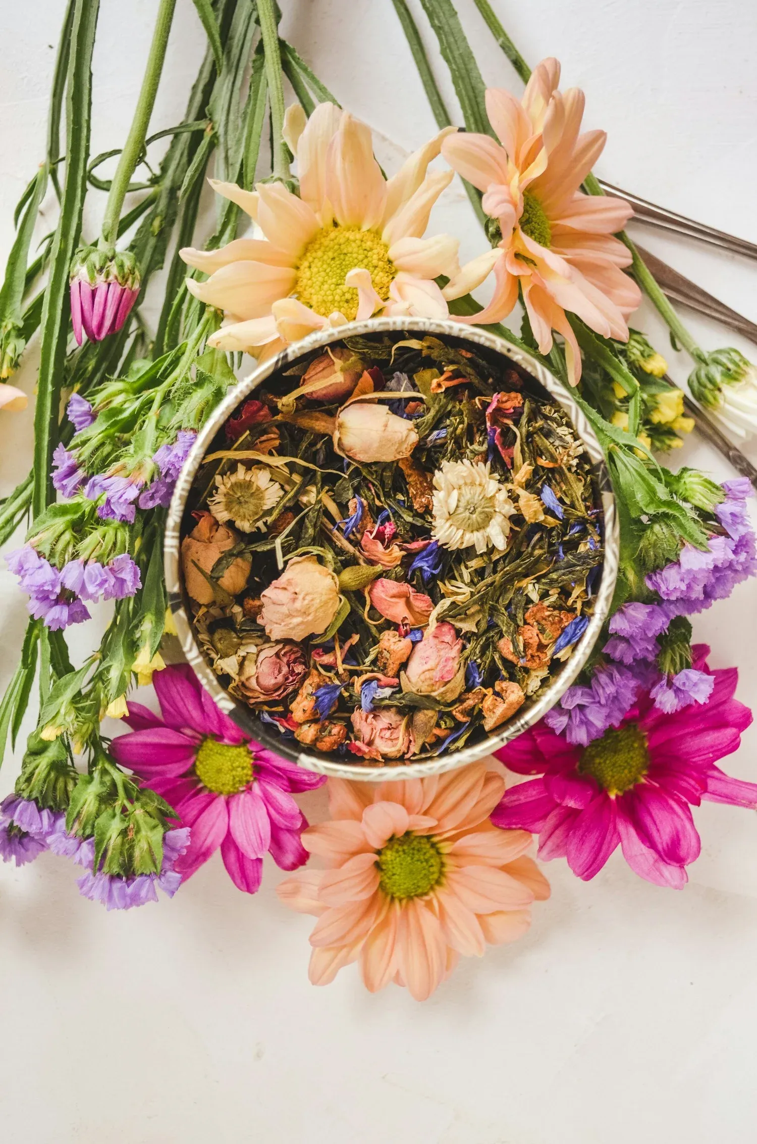 A bowl of dried herbal tea surrounded by bright fresh flowers