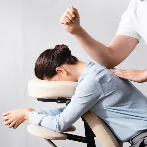 A woman relaxing forward in a massage chair while a therapist works on her shoulders