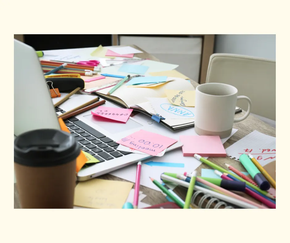 A cluttered desk covered with sticky notes, markers, a laptop and coffee mugs