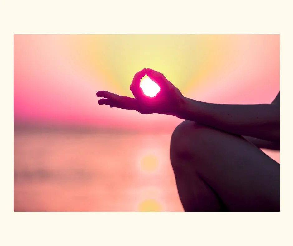 A silhouette of hands in a meditation pose in front of a pink sunset