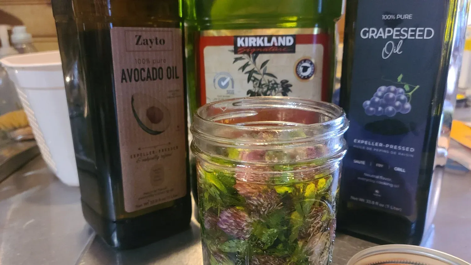 Jars of red clover blossoms infusing in avocado and grapeseed oil
