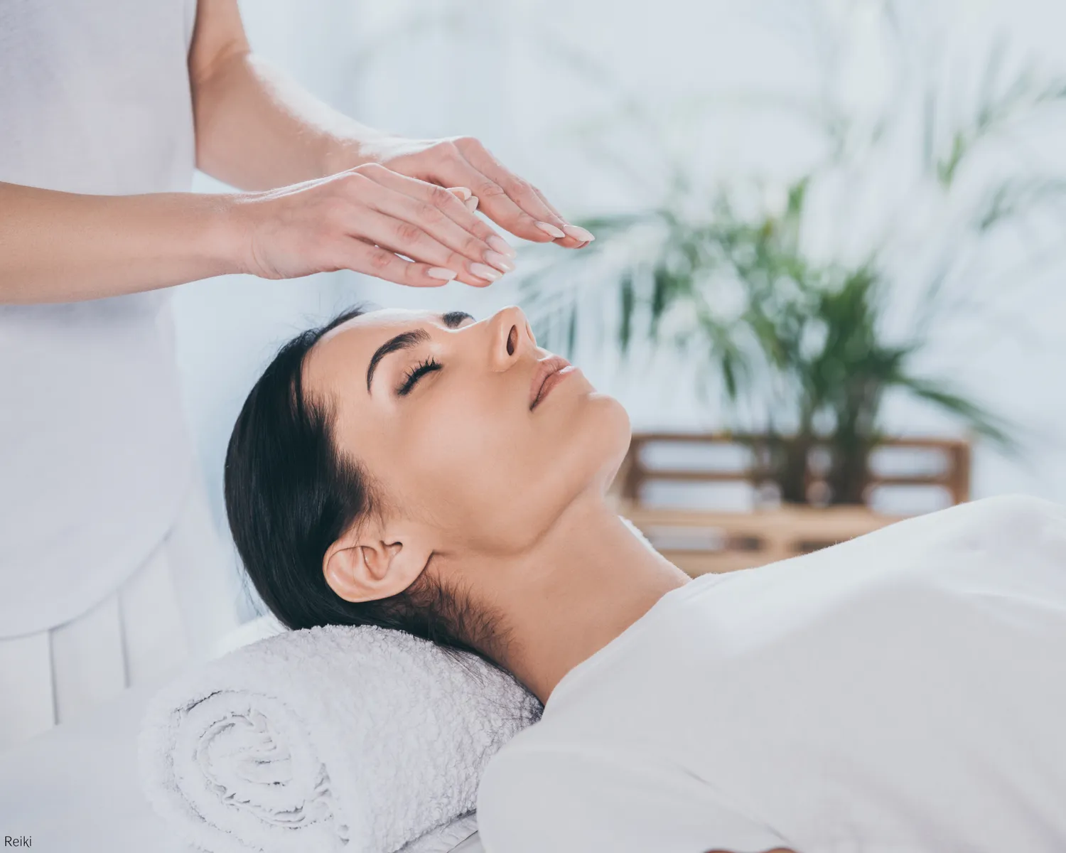 A practitioner holding her hands above a relaxed client’s head during Reiki