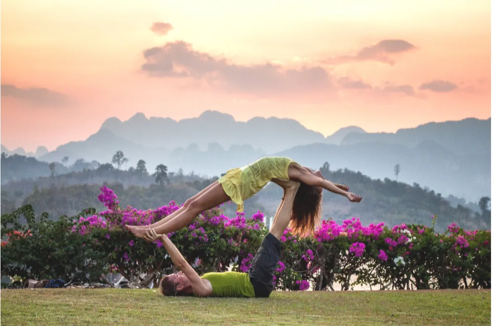 Two people doing partner acrobatic yoga in front of mountains at sunset