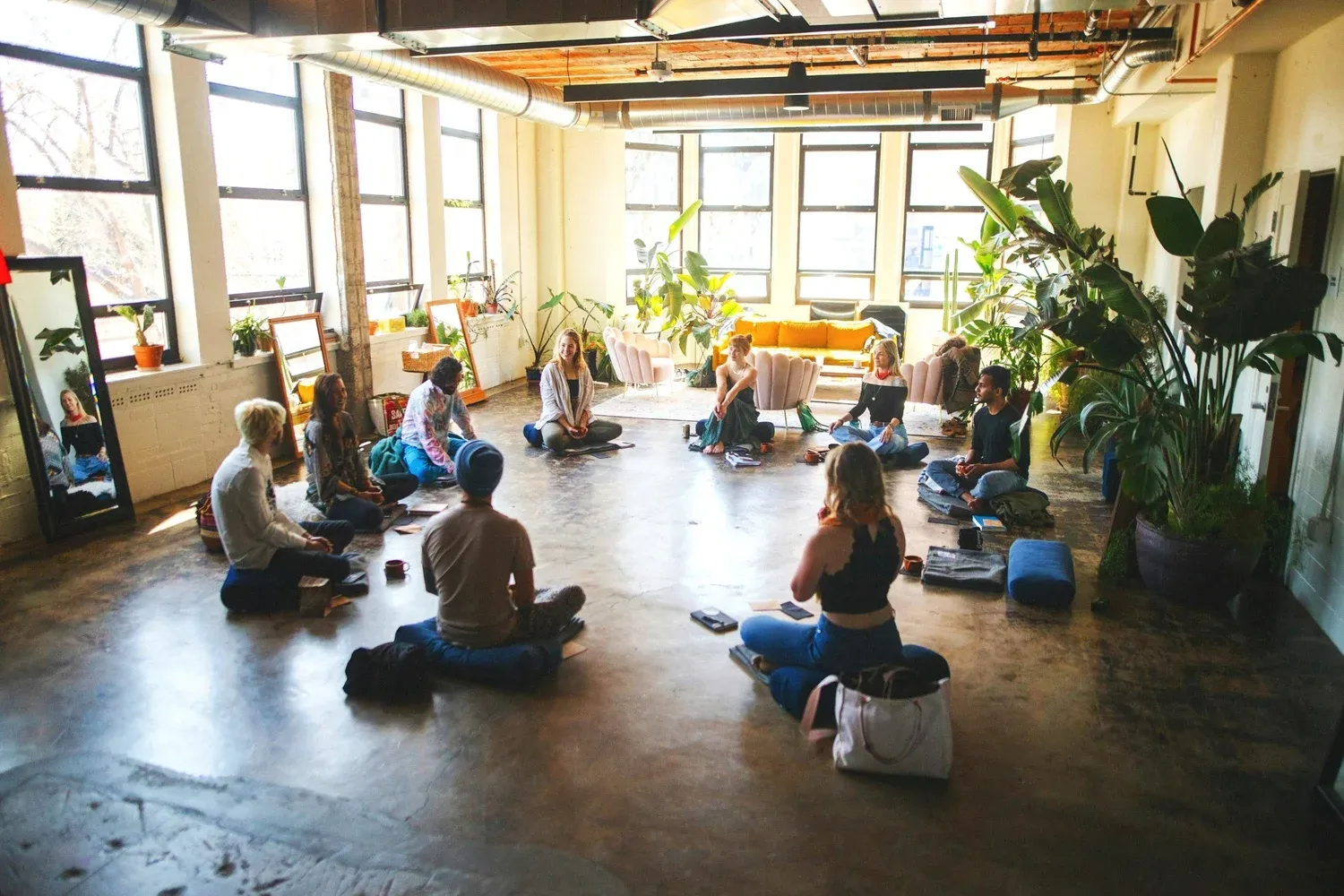 A group sitting on yoga mats in a bright studio filled with plants