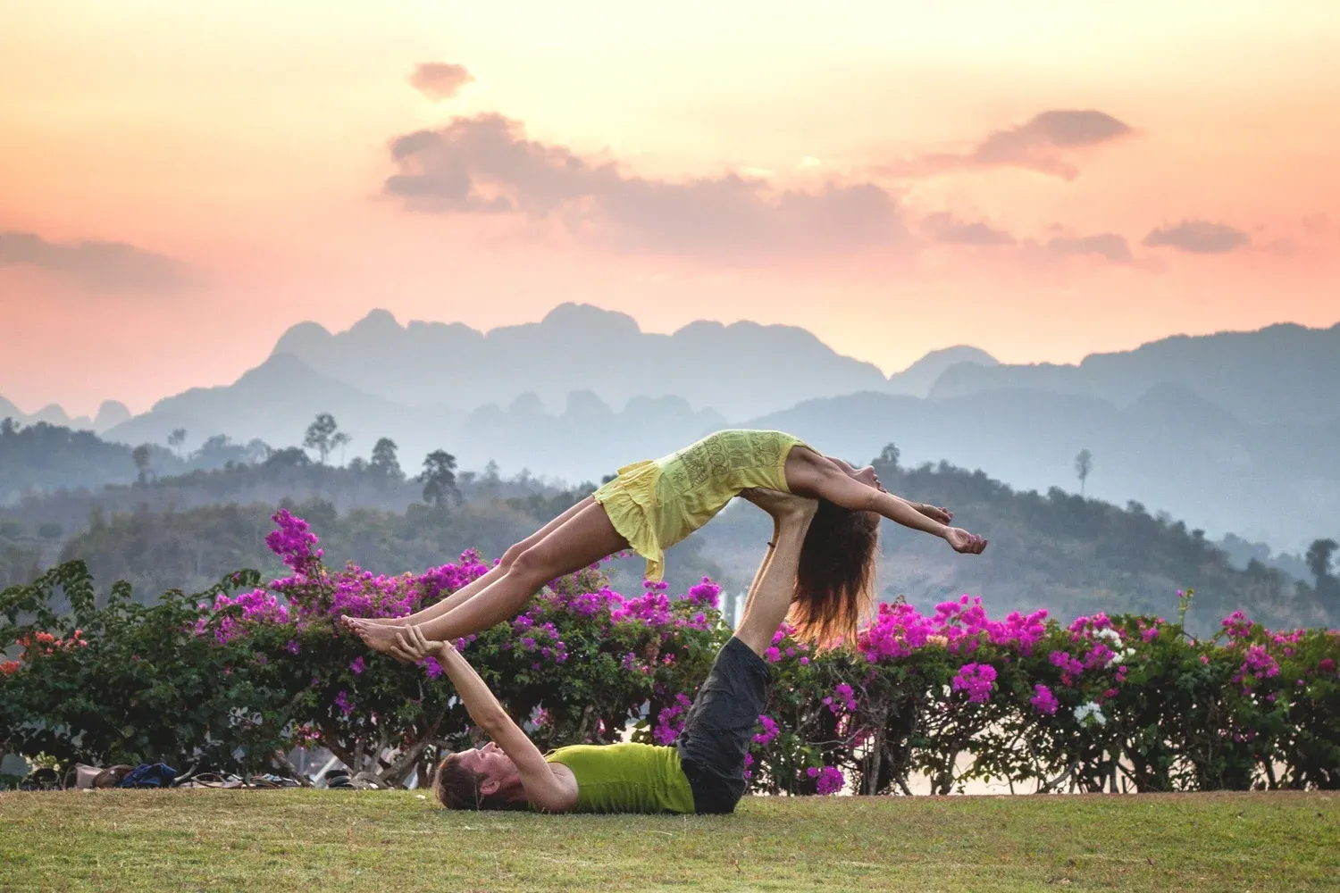Two people doing partner acrobatic yoga in front of mountains at sunset