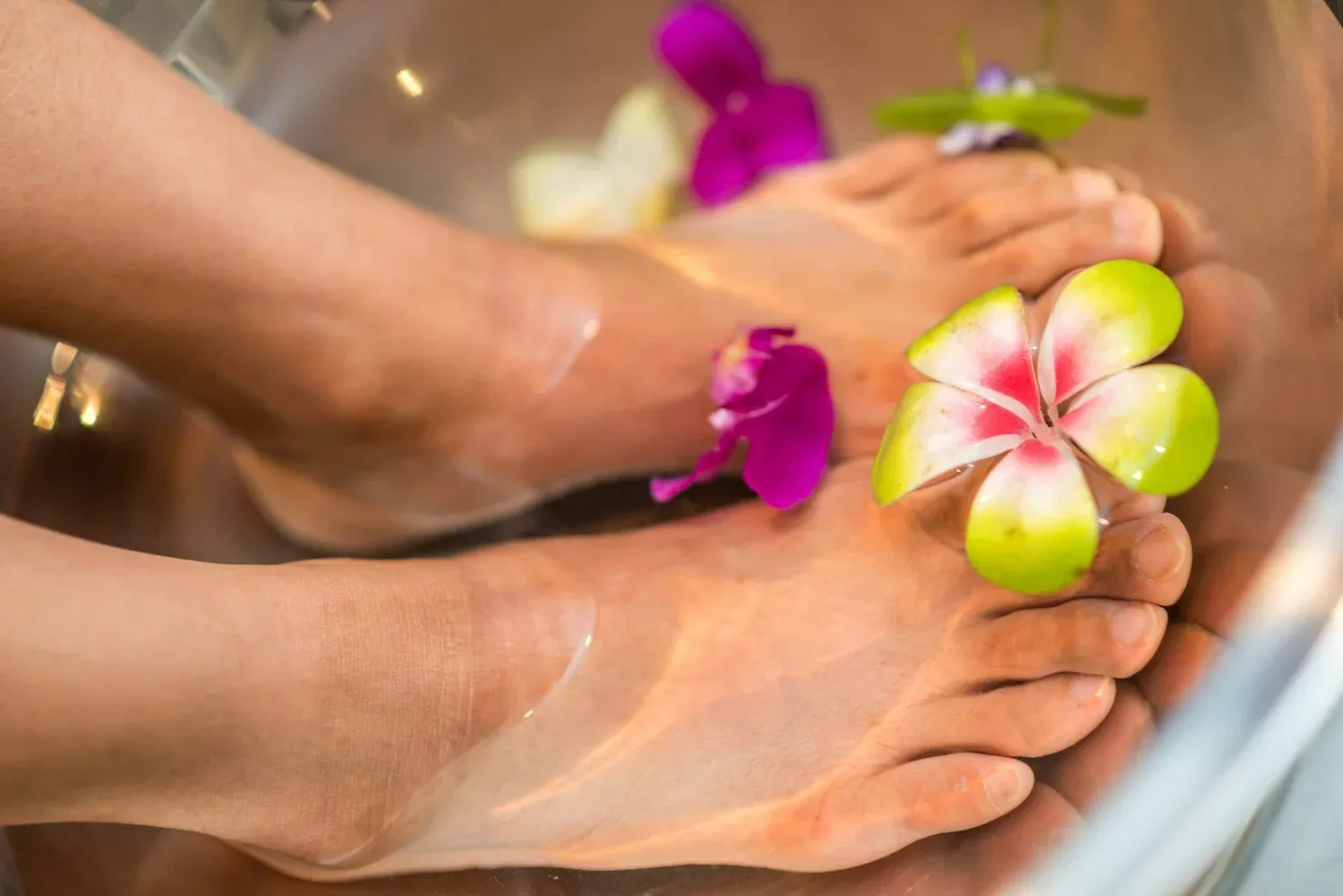 Bare feet resting in a bowl of water with bright tropical flowers
